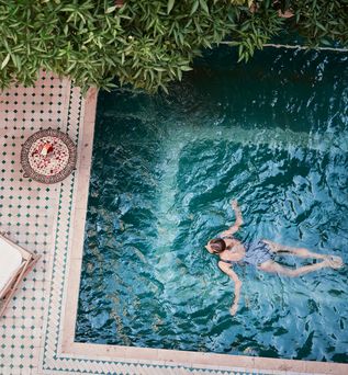 Frau schwimmt in einem Pool; Neben dem Pool, auf der Terrasse steht eine Liege