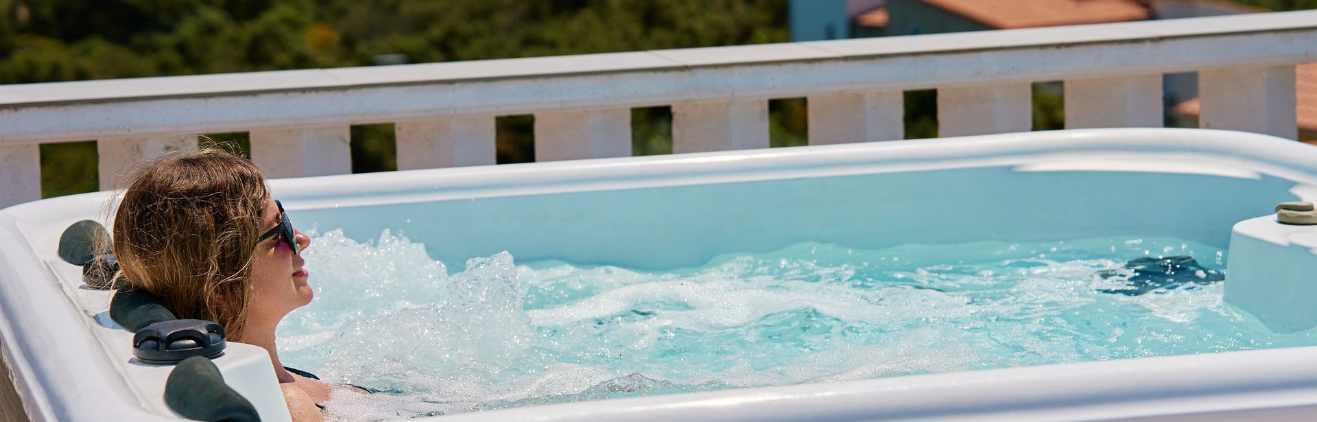 Eine Frau liegt entspannt im Whirlpool, im Hintergrund sind Häuser zu sehen