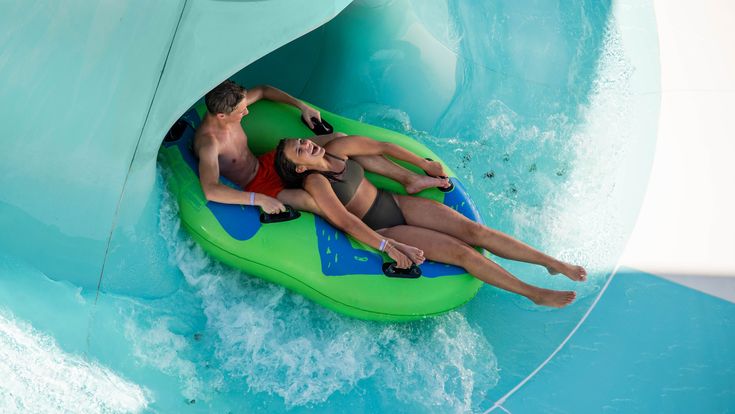 Zwei Personen auf einem Reifen von oben, sie rutschen auf einer Wasserrutsche und schauen nach oben