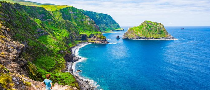 Ein Junge steht erhöht auf einem Hügel, vor ihm das Meer. Im Hintergrund sieht man grüne Wiesen und eine kleine Insel im Meer