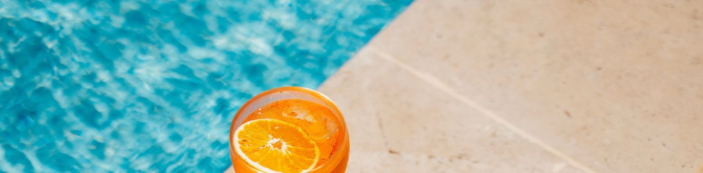 Ein Oranges Getränk steht am Rand eines Pools