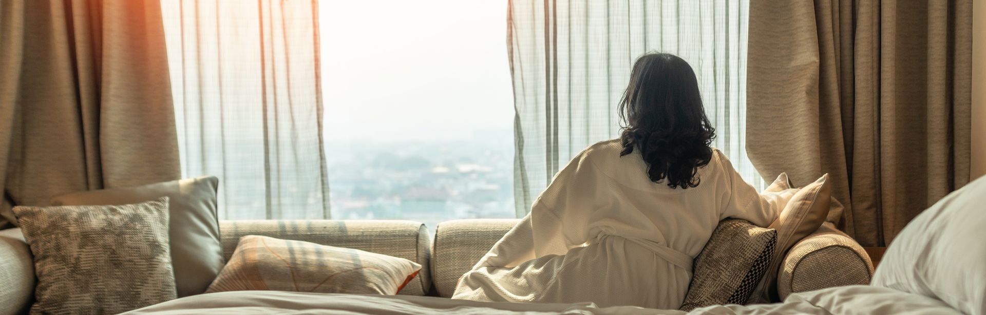 Frau sitzt in Ihrem Hotelzimmer auf dem Sofa und schaut aus dem Fenster
