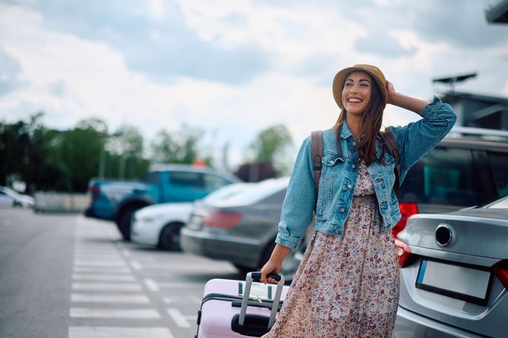 Eine lachende Frau zieht ihren Koffer über einen Parkplatz