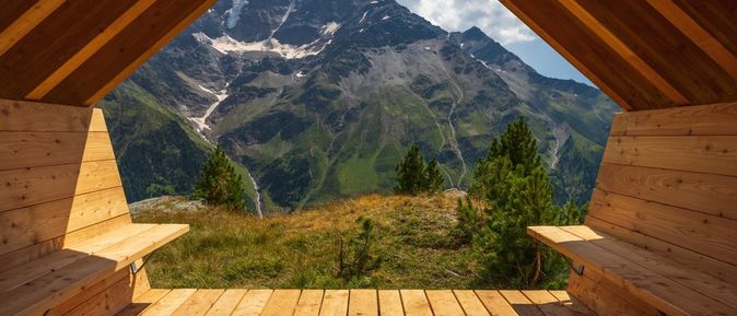 Aus einer Holzhütte mit zwei Bänken schaut man auf eine beeindruckende Berglandschaft