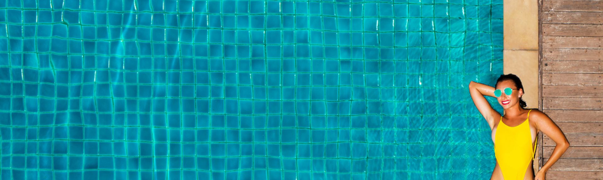 Ein großer Pool, am Rand liegt eine Frau im gelben Badeanzug und einer Sonnenbrille