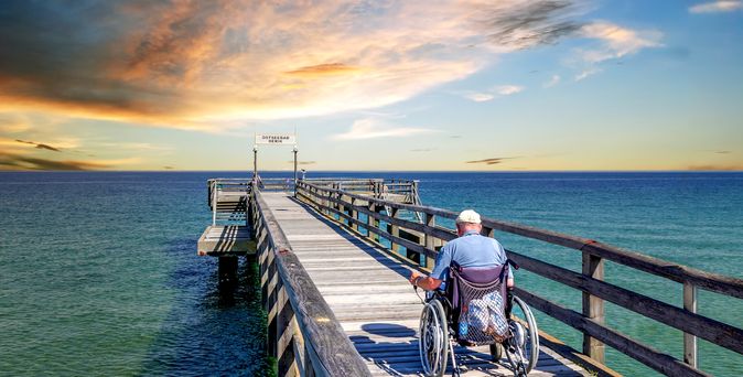Mann im Rollstuhl auf einer Seebrücke am Meer