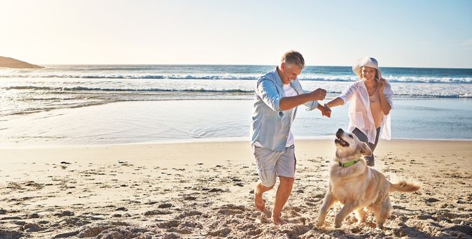 Eine Frau und ein Mann spielen am Strand mit einem Hund 