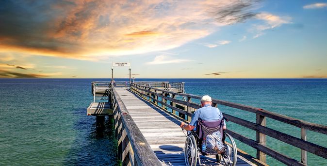 Mann im Rollstuhl auf einer Seebrücke am Meer