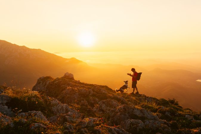Mann und Hund wandern zusammen in den Bergen bei Sonnenuntergang
