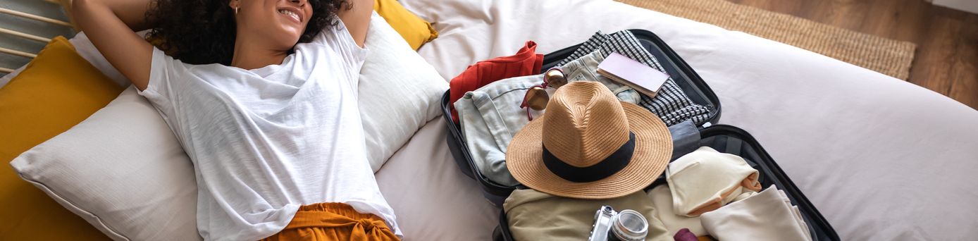 Frau liegt auf einem Bett neben einem gepackten, offenen Koffer