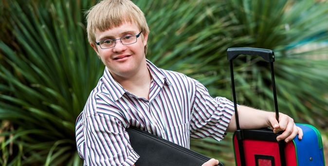 Junger Mann mit einem Koffer und einer Tasche in der Hand umgeben von Pflanzen