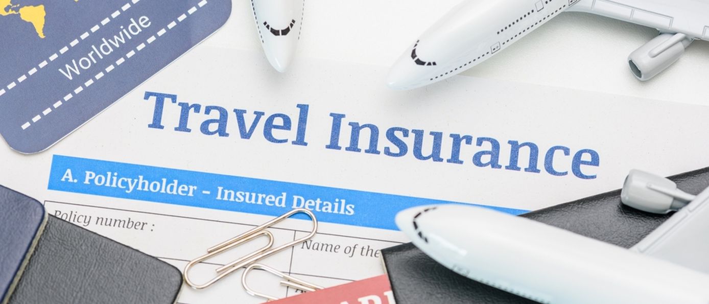 In der Mitte des Bildes steht "Travel Insurance" darum liegen mehrere Büroklammern, Reisepässe und mehrere kleine Flugzeuge