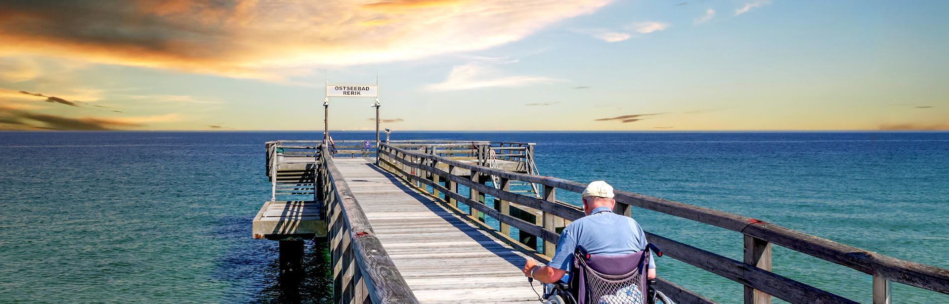 Mann im Rollstuhl auf einer Seebrücke am Meer