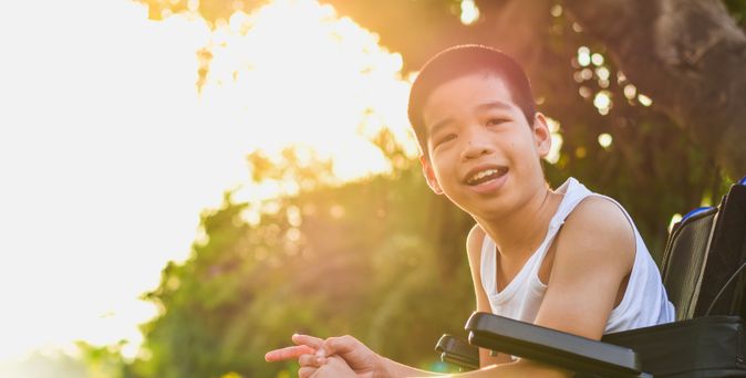 Junge im Rollstuhl in der Natur lächelt in die Kamera