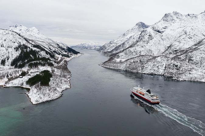 Ein Kreuzfahrtschiff fährt durch einen Fjord, umgeben von schneebedeckten Bergen und winterlicher Landschaft.