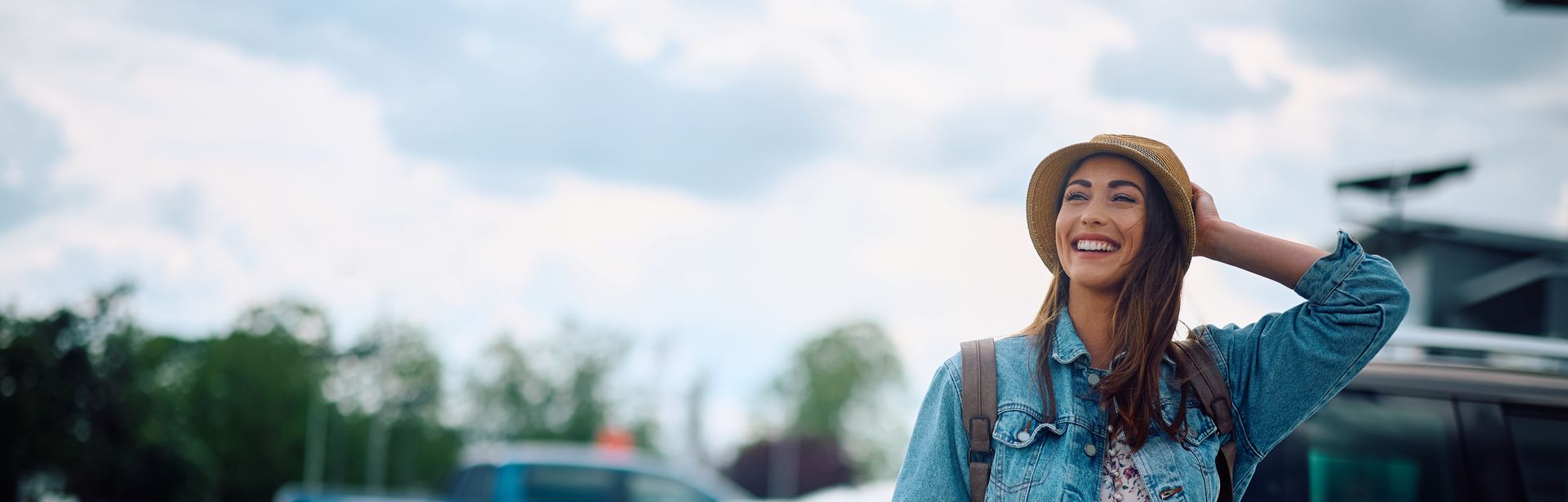 Eine lachende Frau zieht ihren Koffer über einen Parkplatz