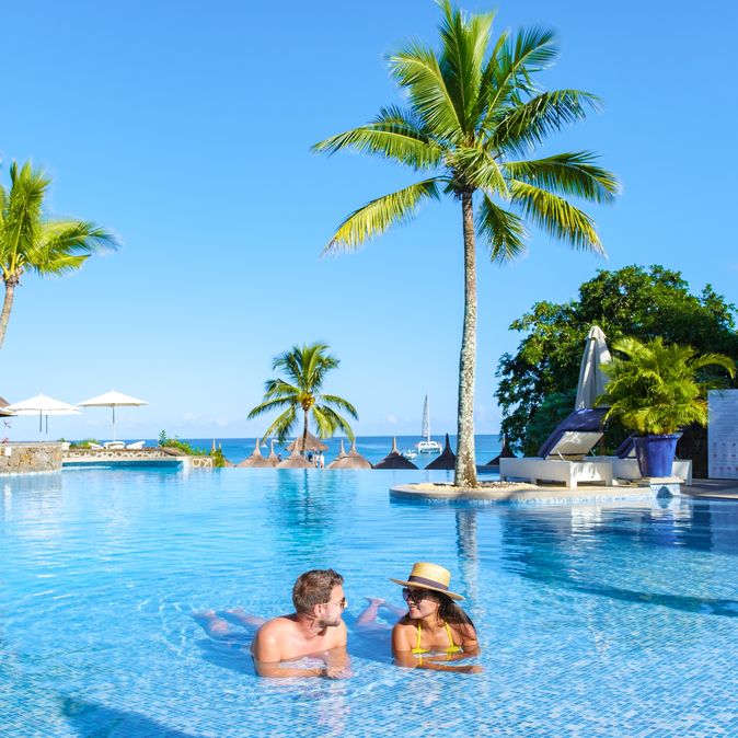 Zwei Personen liegen im Pool umgeben von Palmen