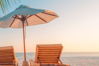 Zwei Liegen mit einem Sonnenschirm stehen unter Palmen am Strand