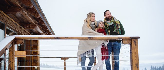Familie steht in Winterklamotten auf der Terrasse eines Balkons während Schnee liegt