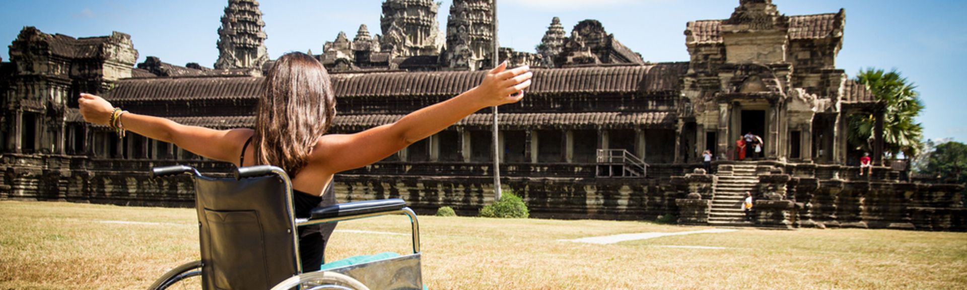 Frau im Rollstuhl vor einem Tempel und hebt die Arme