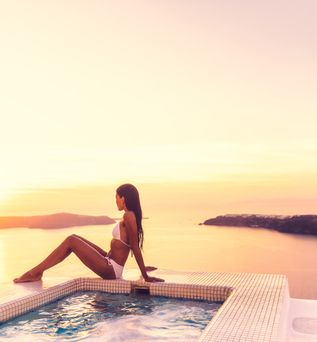 Eine Frau sitzt bei Sonnenuntergang auf dem Rand eines Whirlpools. Im Hintergrund ist ein Gewässer zu sehen