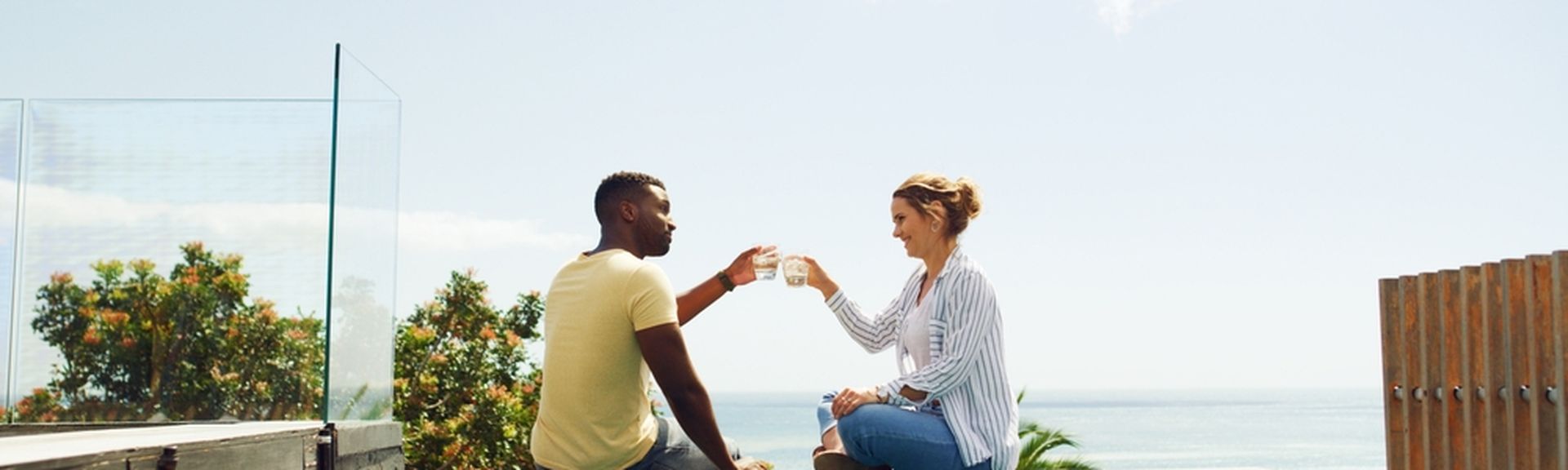Eine Frau und ein Mann sitzen am Pool und stoßen mit Ihren Getränken an