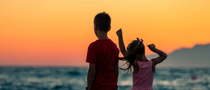 Zwei Kinder schauen bei Sonnenuntergang aufs Meer