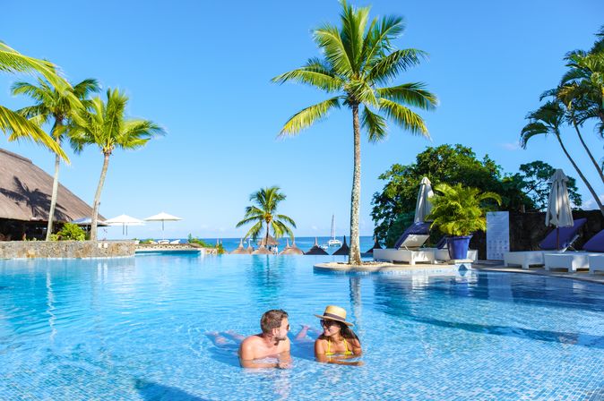 Zwei Personen liegen im Pool umgeben von Palmen