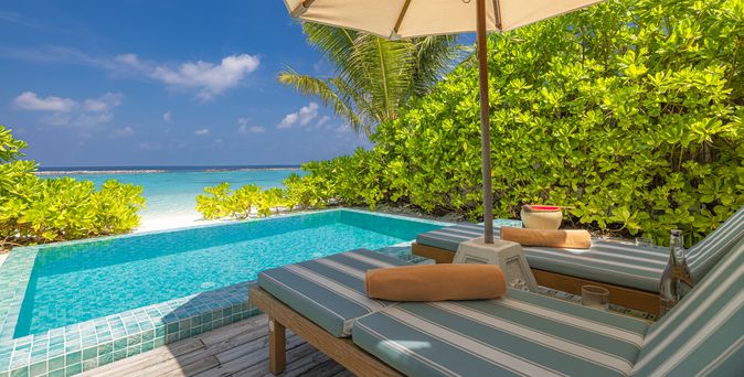 Zwei Liegen unter einem Sonnenschirm, vor einem kleinen Pool