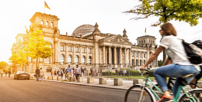 Eine Frau fährt bei Sonnenschein auf dem Fahrrad am Berliner Bundestag vorbei