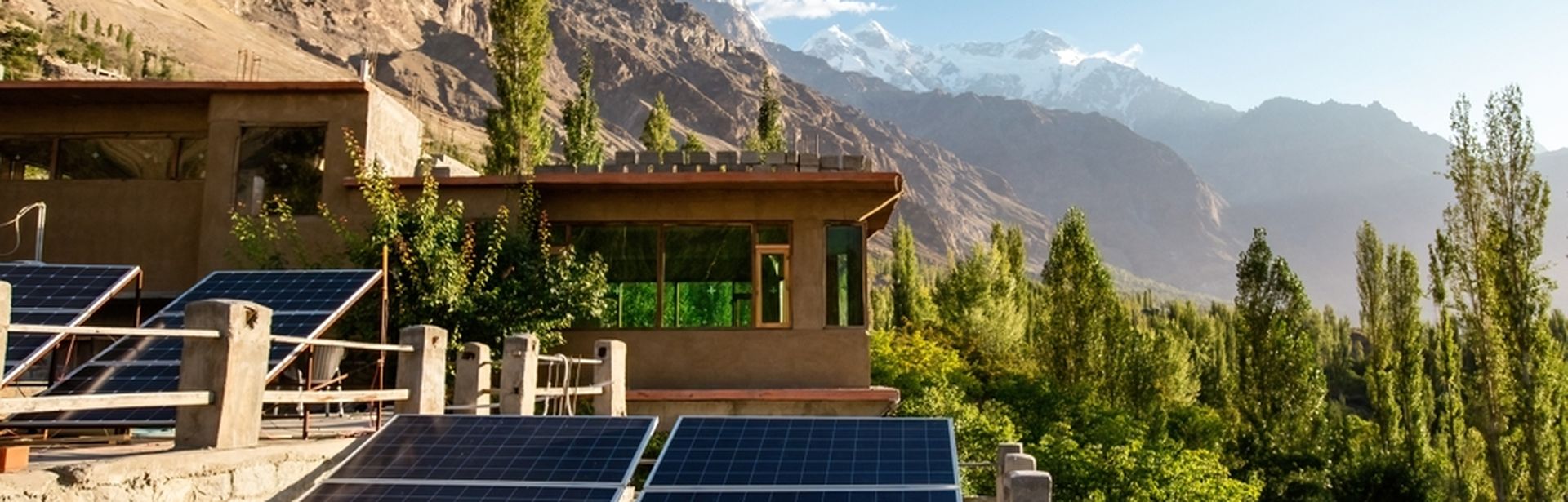 Eine Naturlandschaft mit Bergen und Bäumen, im Vordergrund ein Haus mit mehreren Solarplatten