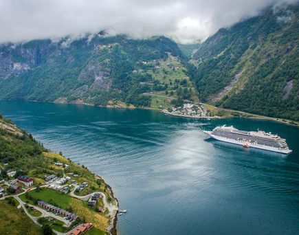 Ein Kreuzfahrtschiff fährt durch einen tiefen, von grünen Bergen gesäumten Fjord mit einem kleinen Dorf im Vordergrund.
