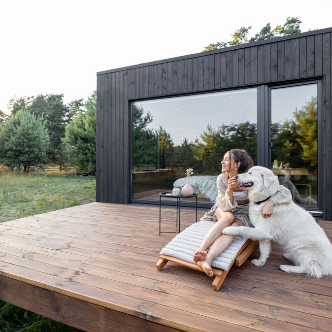 Eine Frau sitzt mit Ihrem Hund auf der Terrasse von einem Ferienhaus