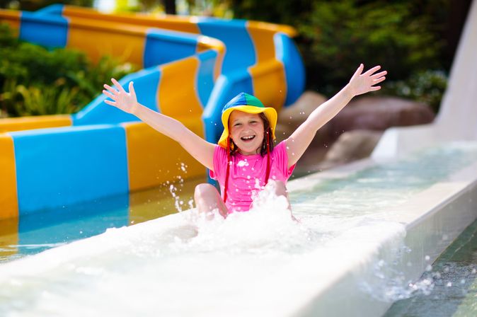 Ein glücklich aussehendes Kind rutscht durch eine Wasserrutsche und hebt die Arme