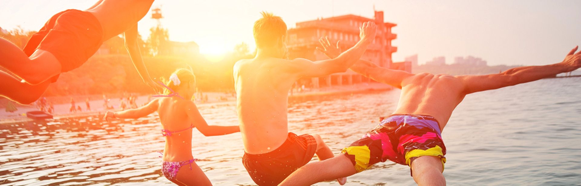 Vier Personen springen bei Sonnenuntergang ins Meer