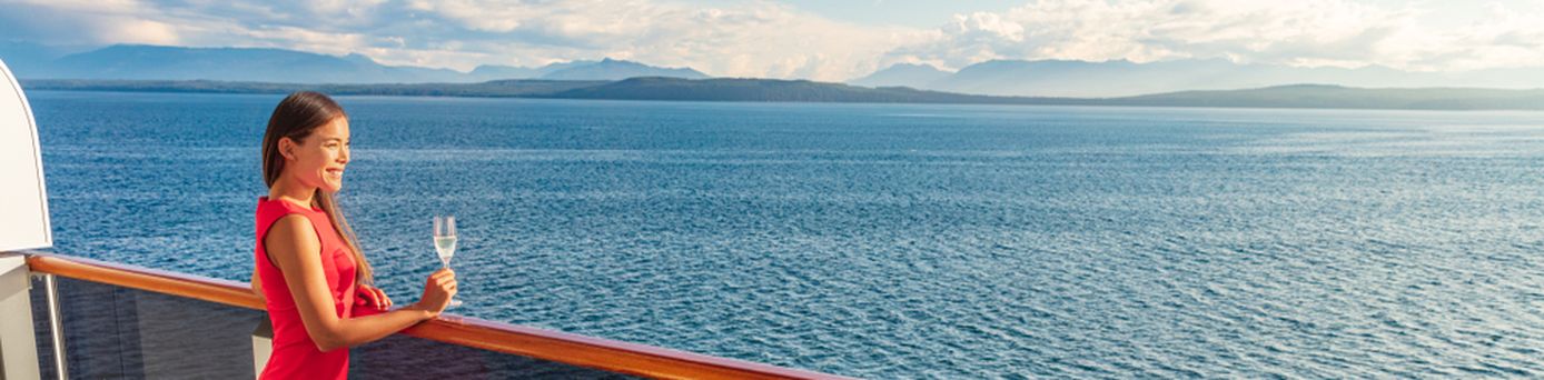 Eine Frau steht mit einem Glas Sekt auf einem Balkon eines Kreuzfahrtschiffes