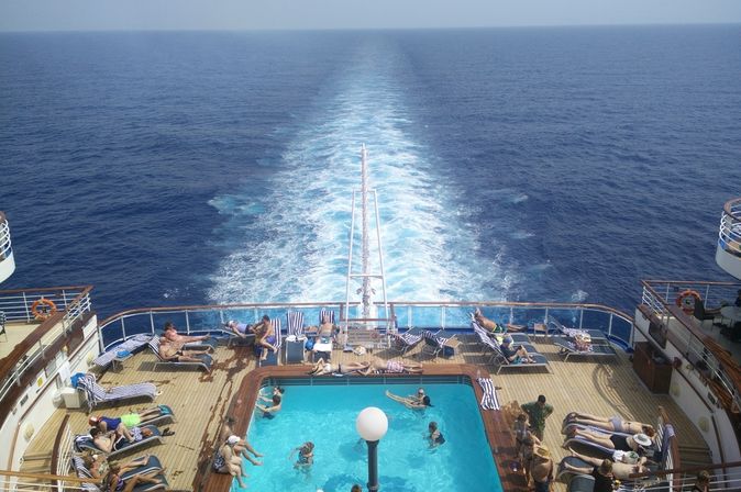 Im Pool am Heck eines Kreuzfahrtschiffes sieht man einige Urlauber schwimmen und sich sonnen