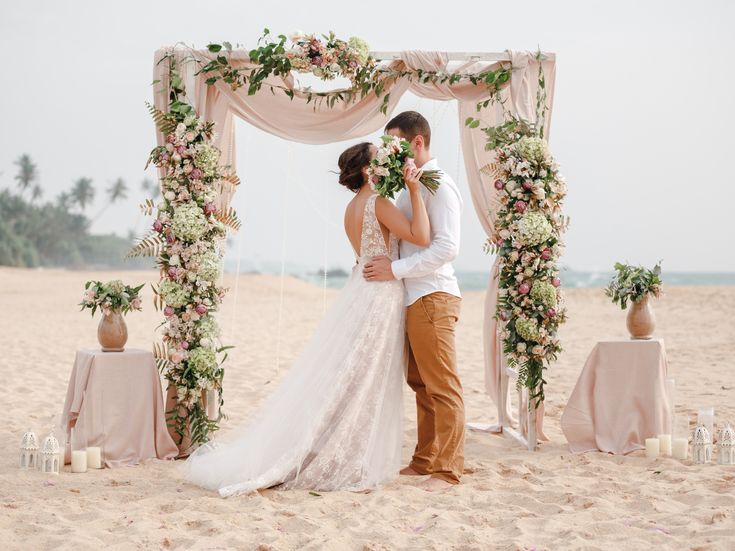 Ein Hochzeitspaar küsst sich unter einem Traubogen am Strand