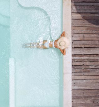Eine Frau mit weißem Sonnenhut lehnt am Rand eines eleganten Pools