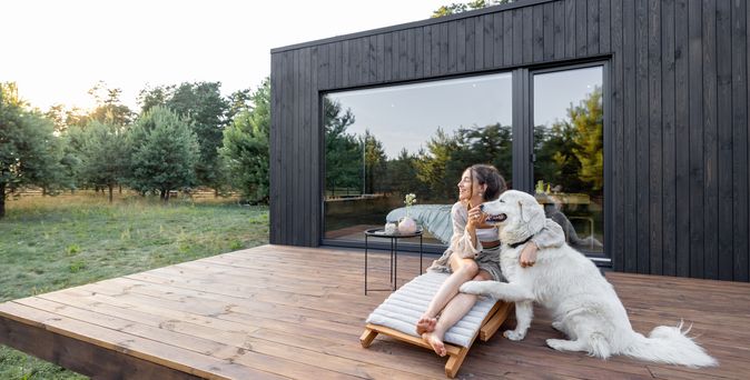 Eine Frau sitzt mit Ihrem Hund auf der Terrasse von einem Ferienhaus