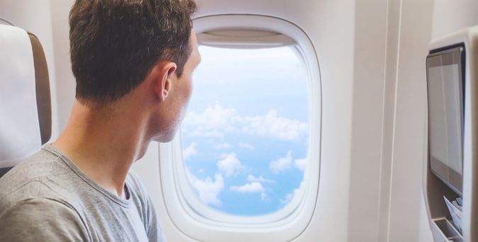 Ein Mann schaut aus dem Flugzeugfenster in den blauen Himmel