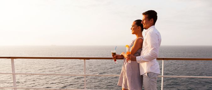 Ein Paar steht auf einem Kreuzfahrtschiff an der Reling und schaut aufs Meer