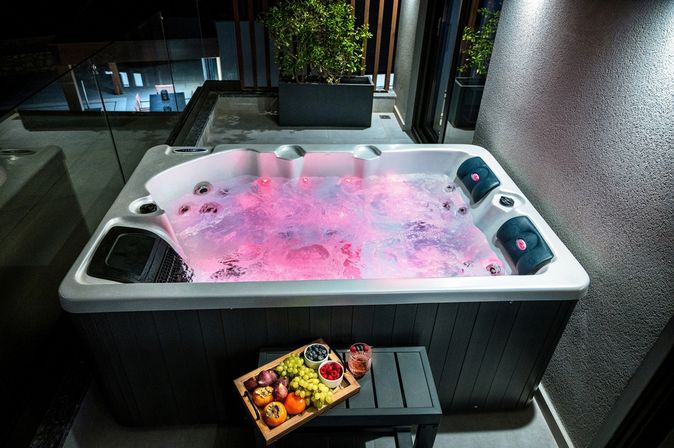 Whirlpool mit roter Beleuchtung im Wasser vor dem ein Tablet mit Obst und ein Getränk auf einem kleinen Tisch steht