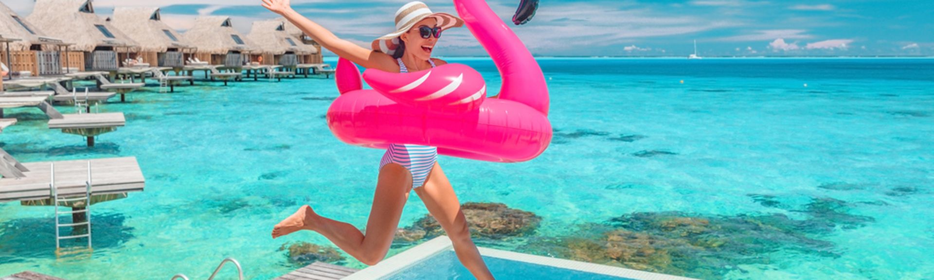 Eine Frau springt lachend mit einem Flamingo Schwimmreifen in einen Pool 