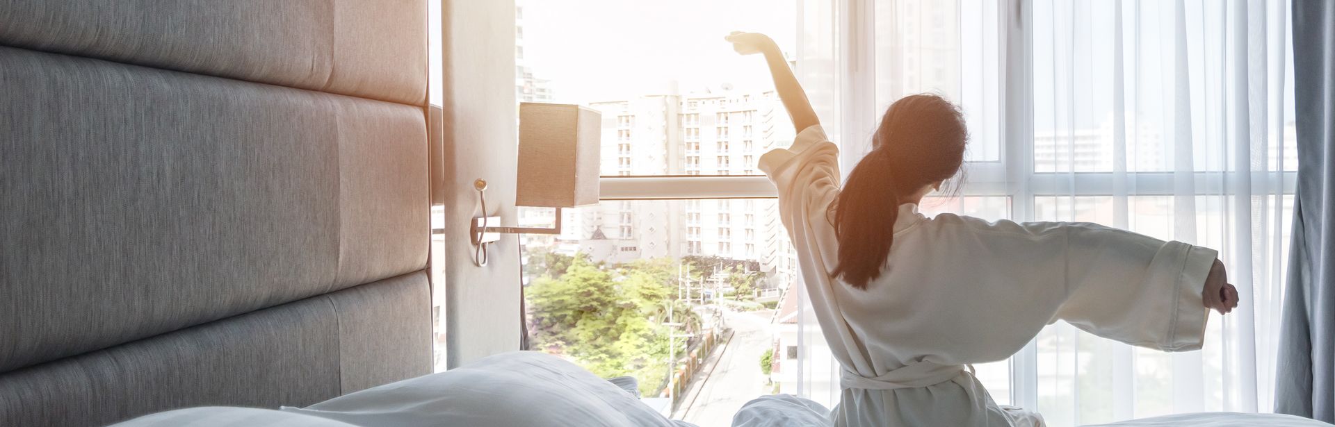 Eine Frau sitzt im Bademantel auf Ihrem Bett und streckt sich 