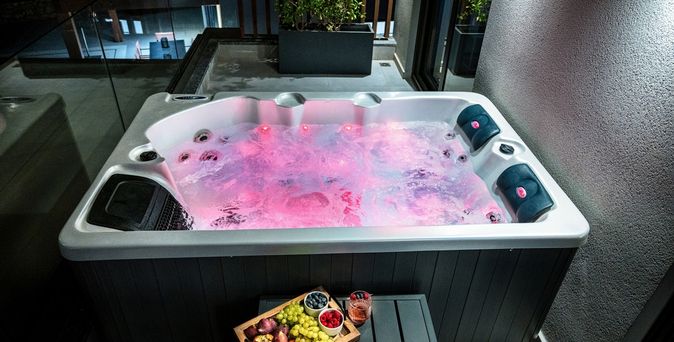 Whirlpool mit roter Beleuchtung im Wasser vor dem ein Tablet mit Obst und ein Getränk auf einem kleinen Tisch steht