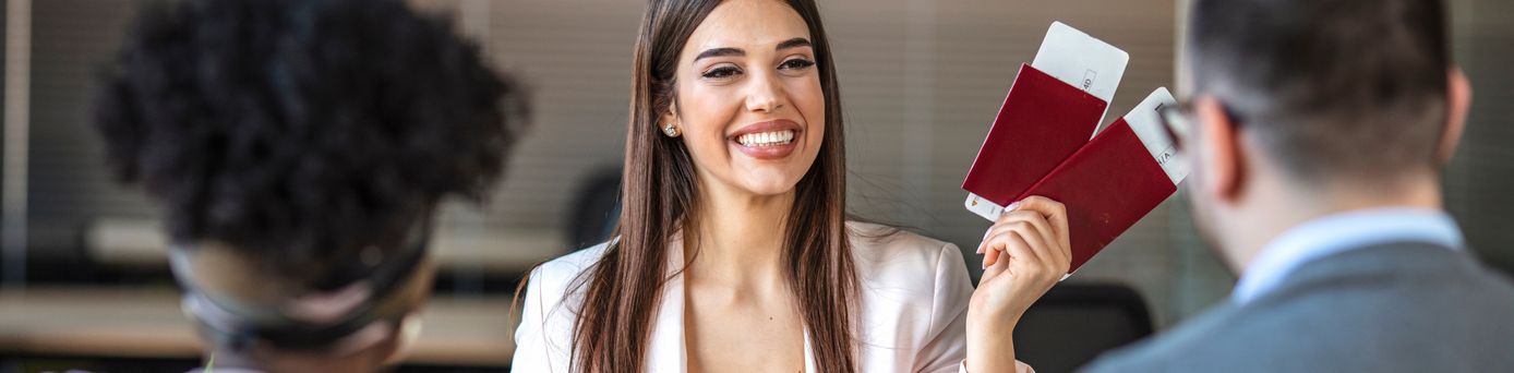 Eine lächelnde Reiseberaterin hält Ihren Kunden zwei Reisepässe mit Flugtickets hin