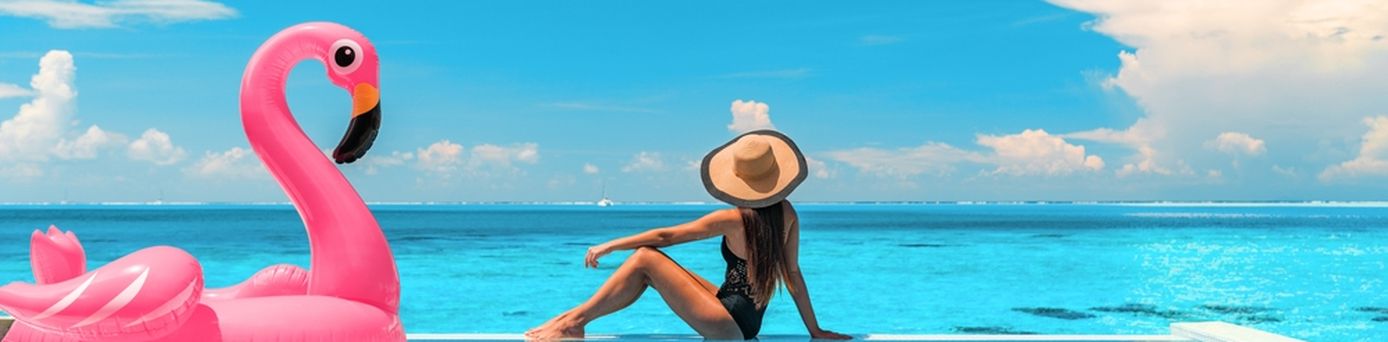 Frau sitzt am Rand eines Pools mit Meerblick, neben Ihr ein aufblasbarer Flamingo