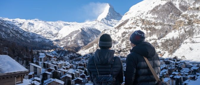 Zwei Personen stehen erhöht und schauen auf ein verschneites Dorf in den Bergen