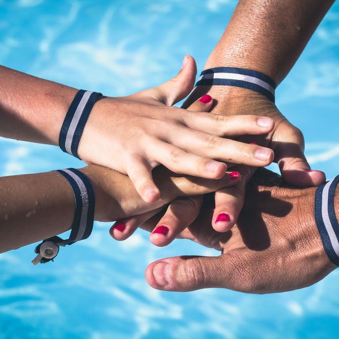 Vier Hände mit Armbändern aufeinander über einem Pool